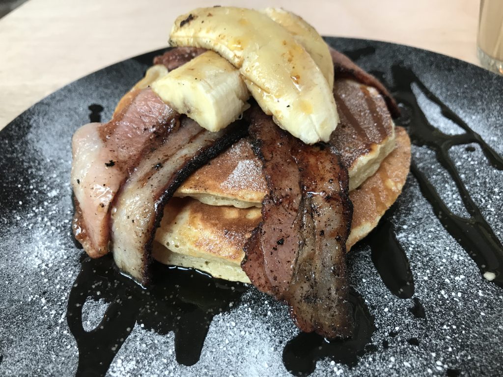 A stack of bacon, banana and maple syrup pancakes at Three Stack